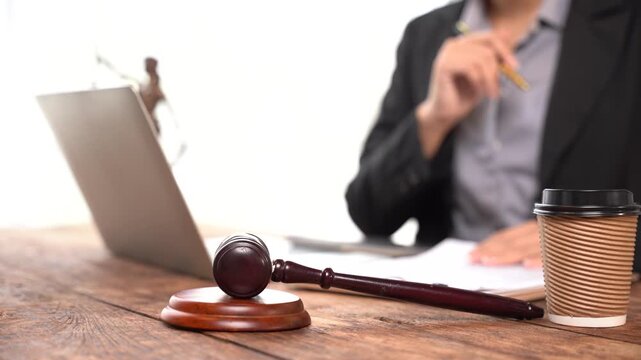 Justice in Focus: A gavel and laptop on a wooden desk, symbolizing legal proceedings and modern legal practice, with a person thoughtfully reviewing documents in the background.