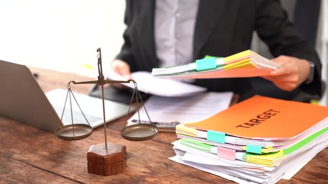 Legal Justice and Hard Work: A legal professional diligently sorts through stacks of documents with a laptop and a balanced scale of justice in the foreground.