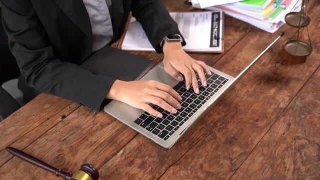 Legal Professional at Work: A person in a suit uses a laptop, surrounded by legal documents and a gavel on a wooden desk, symbolizing the practice of law.