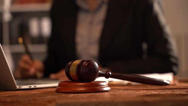 Gavel of Justice: A judge's gavel rests on a wooden desk, with a legal professional in the background diligently working, embodying the essence of law and order.