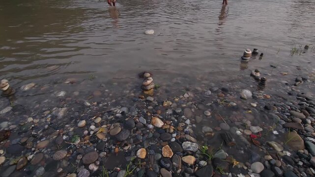 Defocused Sacred River Bathing at Devghat Dham, Nepal, with Balanced River Stones in Foreground, Hindu Pilgrimage, Spiritual Ritual, Peaceful Riverside Landscape and Cultural Heritage