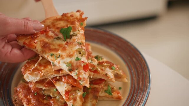 Hand reaches to lift top pizza slice from stacked portions on decorative ceramic plate, with melted cheese stretch, glossy tomato sauce, herb garnish, browned crust, and warm casual dining mood