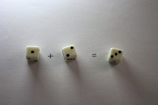An addition math problem shows white dice&mdash;displaying numbers An addition math problem shows white dice&mdash;displaying numbvia their dots&mdash;on a white background, casting shadows. one plus two equals three 