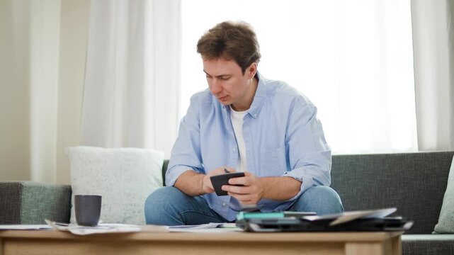 Stressed man calculates household expenses and utility bills with a calculator. Facing financial crisis, economic pressure, inflation, and rising living costs at home. High quality 4k footage