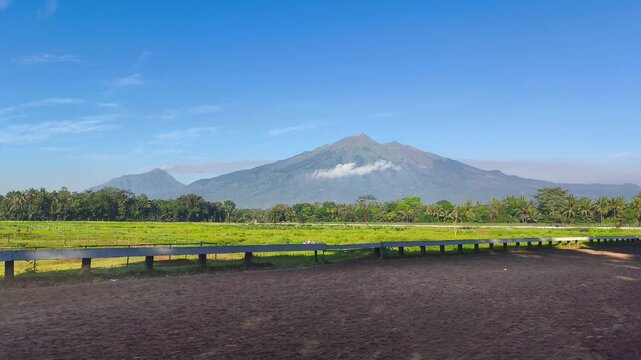 Stunning Mount Merbabu volcano landscape view from a local race track field in Java Indonesia under clear blue sky concept of natural beauty human space adventure freedom and travel background