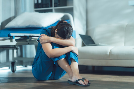 Distress in Scrubs: A healthcare worker, overcome with emotion, sits on the floor of a room, hugging her knees in a moment of deep despair.