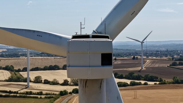 Aerial view of Penny Hill Wind Farm with a large wind turbine nacelle and blades overlooking rural fields and farmland under a clear blue sky in Aston, England, United Kingdom.