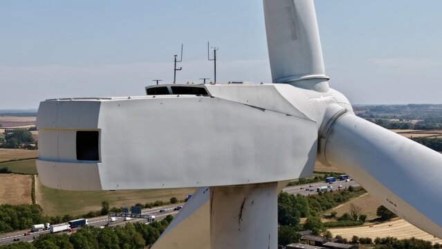 Aerial view of the Penny Hill Wind Farm turbine nacelle and blades with a highway and rural landscape in the background in Aston, England, United Kingdom.
