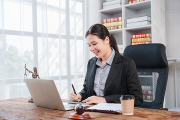 Fototapeta premium Legal Professional at Work: A focused female lawyer, poised and professional in her office, reviews documents on her laptop while taking notes, symbolizing dedication to justice and legal practice.