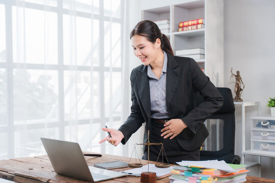 Excited Lawyer in Office: A female lawyer dressed in a formal suit gestures enthusiastically while looking at her laptop, a picture of professional engagement and success.