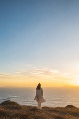 Fototapeta premium Woman standing on a coastal cliff overlooking the ocean at sunset. Peaceful travel landscape with expansive sky, solitude, reflection, and copy space for inspirational concept