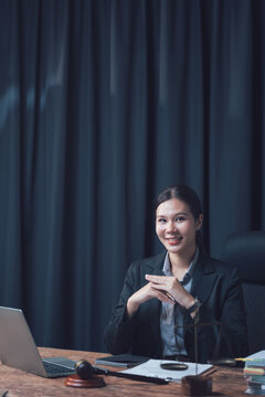Lawyer at Desk: A poised female lawyer sits at her desk in a dimly lit office, a laptop and gavel in view, exuding confidence and professionalism.