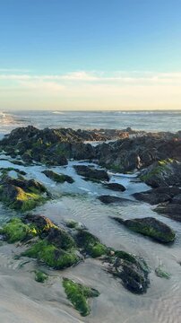 Sea, beach boulders, pebble shore, and waves at sunset. Sea waves breaking on rocks. Sunny beach with dunes and blue sky in Esposende, Portugal.