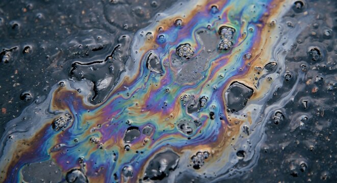 Iridescent oil slick on wet asphalt pavement showing vibrant rainbow colors and swirling patterns from a gasoline spill after rain