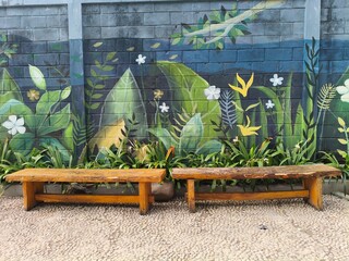 Painted botanical leaf mural on wall behind garden plants and wooden bench © Irvan