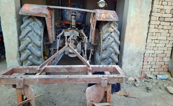 Old rusty tractor parked in a farm shed with attached agricultural plow equipment.