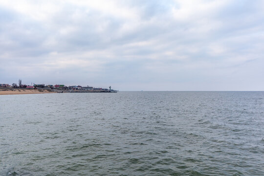 Coastal view showcasing a tranquil sea and a distant shoreline with buildings, set against a backdrop of overcast clouds