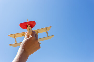 A boy holds a wooden airplane model by the tail and directs the plane towards the blue sky. © Prrrettty
