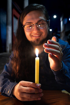 Smiling man holding lit candle shielding flame at night. Candle Day, Colombia