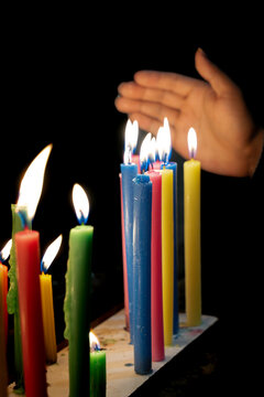 Hand protecting colorful lit candles flame at night vigil. Candle Day, Colombia