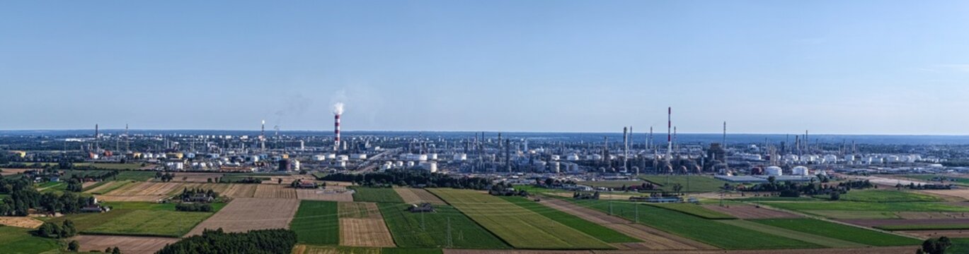 Aerial view of the PKN Orlen refinery complex with its industrial towers and storage tanks surrounded by agricultural fields in Plock, Masovian Voivodeship, Poland.