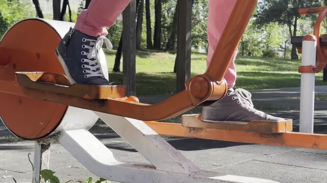 Person exercising on outdoor stepper fitness equipment in public park, performing stepping motion during outdoor workout, active lifestyle, fitness, recreation, healthy living