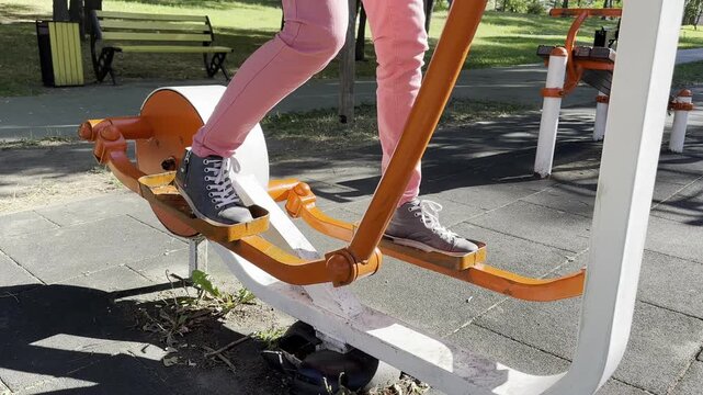 Person exercising on outdoor stepper fitness equipment in public park, performing stepping motion during outdoor workout, active lifestyle, fitness, recreation, healthy living