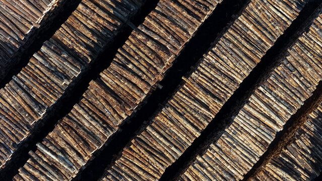 Aerial view of stacked timber logs creating a geometric pattern of wood textures and dark shadows in Nelson, Nelson Region, New Zealand.
