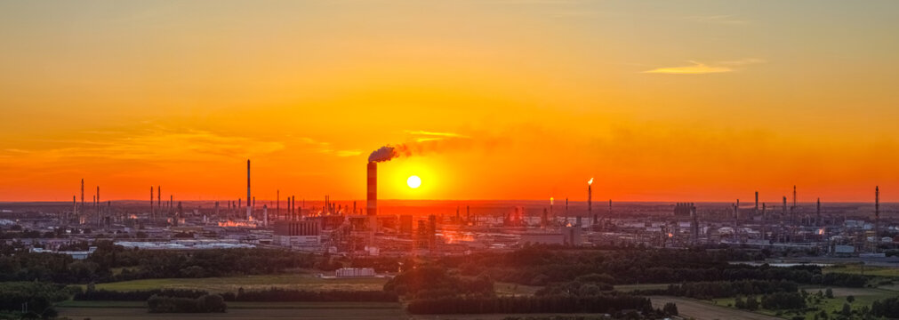Aerial view of the PKN Orlen refinery complex at sunset with industrial chimneys and smoke plumes in Plock, Masovian Voivodeship, Poland.