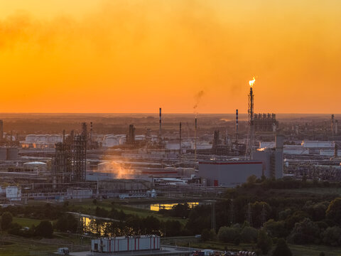 Aerial view of the PKN Orlen industrial complex at sunset, featuring a flare stack, storage tanks, and industrial buildings in Plock, Masovian Voivodeship, Poland.