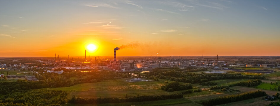 Aerial view of the PKN Orlen refinery in Plock at sunset, with industrial chimneys, storage tanks, and green fields under a golden sky. Plock, Masovian Voivodeship, Poland.