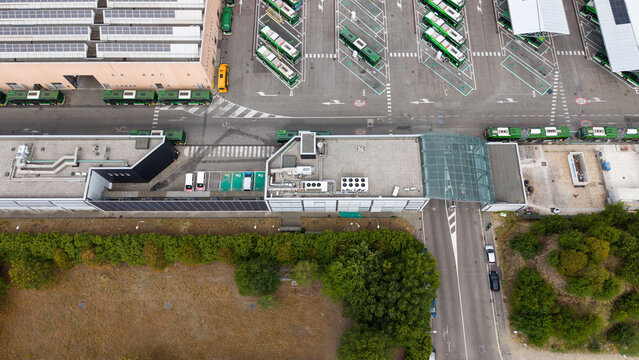 Aerial view of an electric bus depot in Milan featuring rows of parked green buses, modern depot buildings with solar panels, and surrounding urban infrastructure in Milan, Lombardy, Italy.