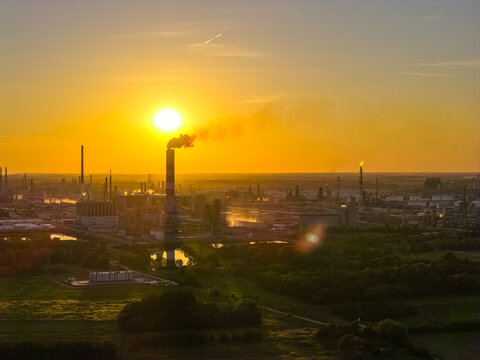 Aerial view of the PKN Orlen refinery complex at sunset with industrial chimneys, storage tanks, and surrounding green fields in Plock, Masovian Voivodeship, Poland.