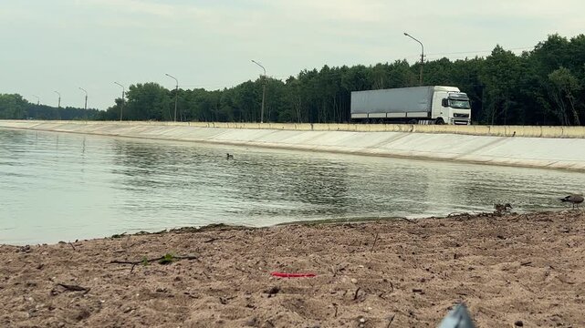 Semi truck reversing along a lakeside road near a reservoir, commercial transport, logistics, vehicle movement, infrastructure, industrial travel.