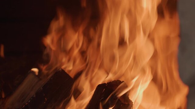 Fire burning, in indoor fireplace, with wood, ashes, from a close-up perspective, with orange, yellow accents, and warm cozy mood, showing nearby objects and surrounding setting, nearby objects.