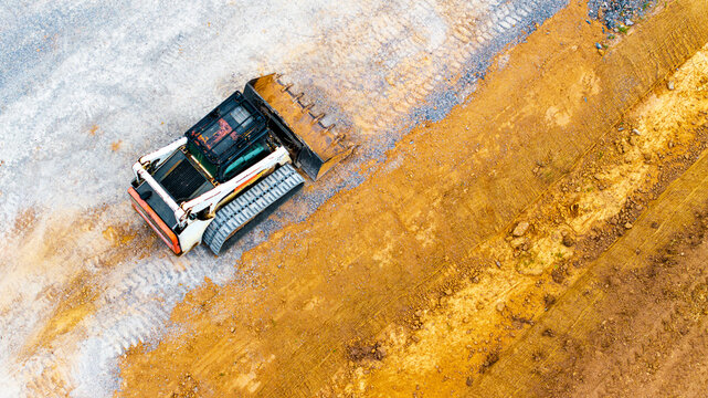 Aerial view of a skid-steer loader working on a new road construction site with exposed earth and tire tracks in Germany.