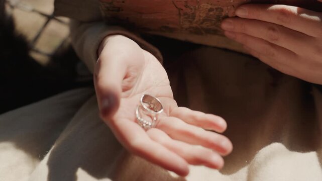 Close-up motion showing child holding two clear glass marbles while other hand steadies worn hardcover book on lap; gentle tilt and slight shift create quiet sense of balance and curiosity