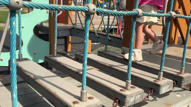 Child hesitating on suspended wooden playground steps, cautious play, balance challenge, childhood fear, outdoor recreation, motor development.