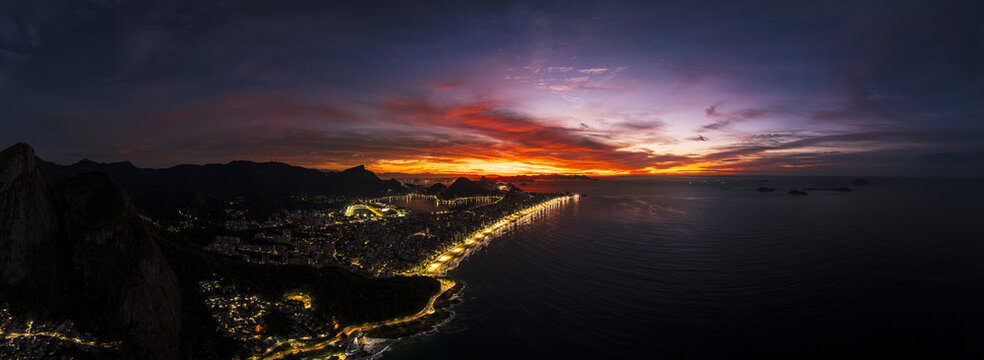 Aerial view of the illuminated coastline of Rio de Janeiro at sunset, featuring the vibrant city lights, dark mountains, and the vast Atlantic Ocean, Rio de Janeiro, Rio de Janeiro, Brazil.