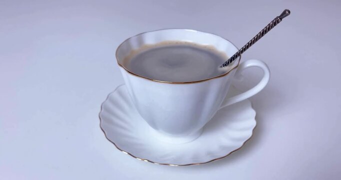 White porcelain teacup filled with hot black coffee sitting on matching saucer on table.