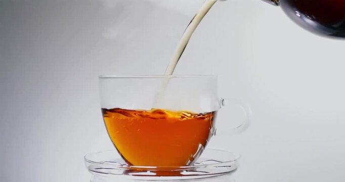 Fresh hot tea pouring into transparent glass cup with steam rising on light background hd.