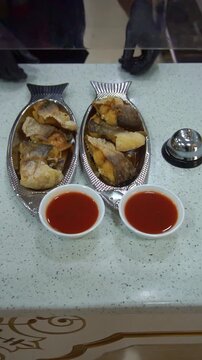Chef serving fried fish dishes on fish-shaped plates with tomato sauce bowls at restaurant counter