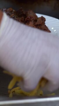 Chef in white gloves adding crispy french fries to a traditional meat and rice plate, slow motion vertical video.