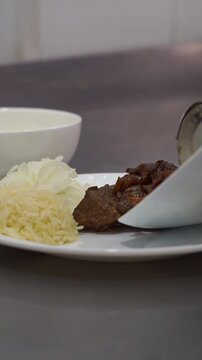 Chef putting delicious roasted meat next to rice and sliced onions on a white plate, slow motion vertical video.