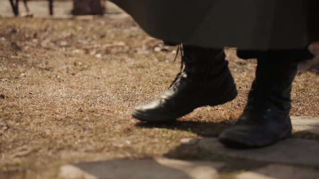 Feet in boots standing, in outdoor possibly historical setting with stone and dirt, with boots, stone pavement, dirt, from a close-up of feet and lower legs perspective, with black, brown accents.