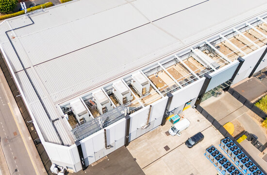 Aerial drone image of a modern data centre roof, with existing industrial cooling HVAC units alongside pre-built empty framework for expansion