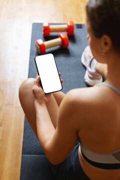 Active woman on fitness mat holding a smartphone with a plain white screen for mobile app mockup