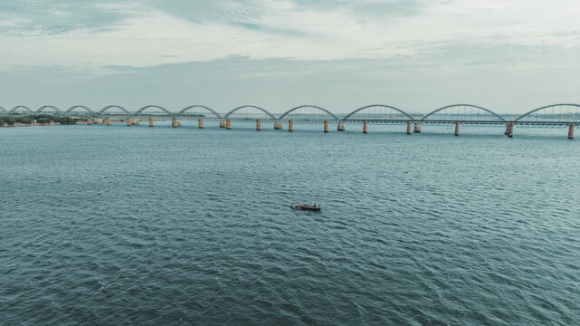 Aerial view of the Godavari Arch Bridge spanning the wide river with a small boat floating on the water in Rajamahendravaram, Andhra Pradesh, India.