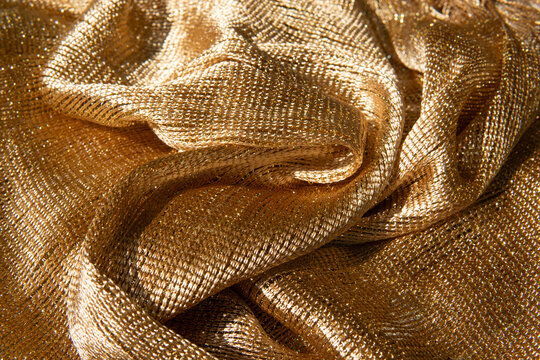 A shimmering golden metallic fabric with rich woven texture and elegant draped folds