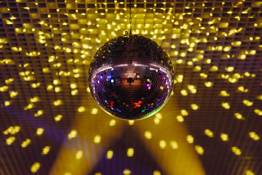 disco ball with mirror surface and bright rays, yellow purple light, hanging on ceiling, night party background